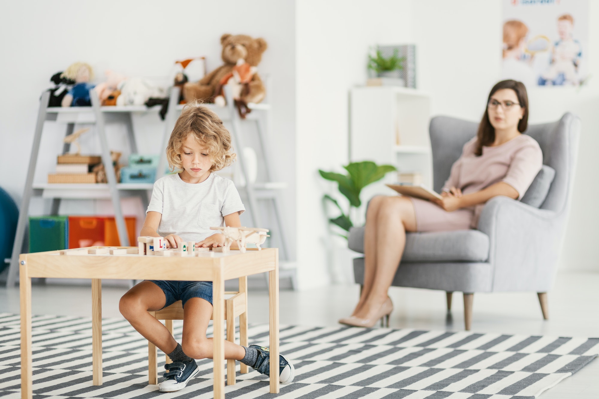 Boy playing at desk in the classroom while psychologist analysin